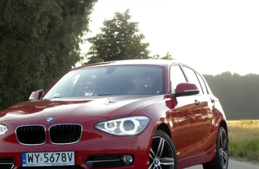 Czerwone BMW 118d na tle drzew i pól.