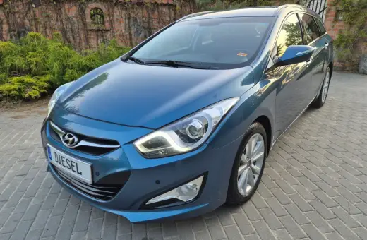 Niebieski Hyundai i40 1.7 CRDi na podjeździe z kostki brukowej, z tyłu ceglany mur porośnięty bluszczem.