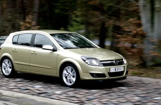 Złoty Opel Astra 1.7 CDTI w ruchu, na tle rozmytego lasu.