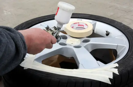 Ręka trzymająca pistolet natryskowy podczas polerowania felg aluminiowych. Taśma maskująca zabezpiecza oponę.