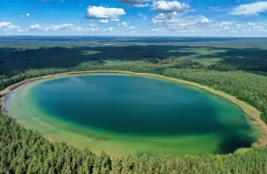 Widok z lotu ptaka na owalne jezioro o turkusowej wodzie, otoczone gęstym lasem. To najczystsze jezioro w Polsce, zachwyca przejrzystością.