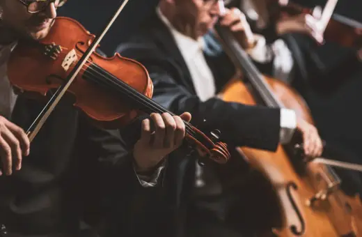 Muzycy w eleganckich strojach grają na instrumentach smyczkowych. W centrum uwagi skrzypek, a w tle wiolonczela. To piękny intro do koncertu.
