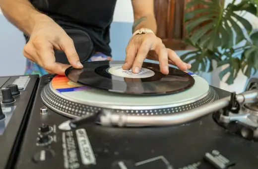 DJ kładzie winylową płytę na gramofonie. Kolorowy **cover** pod nią dodaje klimatu.