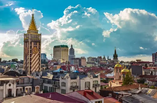 Widok na stolicę Adżarii, Batumi, z charakterystyczną wieżą zegarową i złotymi kopułami cerkwi pod błękitnym, chmurowym niebem.