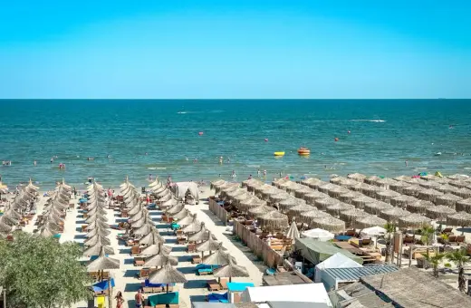 Słoneczna plaża w Rumunii, pełna leżaków i parasoli. Ludzie kąpią się w morzu, idealne miejsce na wakacje.