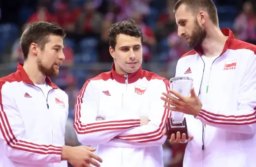 Trzech siatkarzy w strojach z biało-czerwoną flagą Polski. Jeden z nich trzyma puchar, symbolizujący, kto jest aktualnym mistrzem świata w siatkówce.