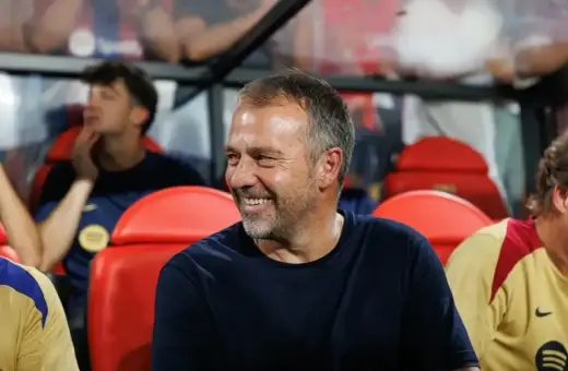 Uśmiechnięty trener Barcelony, siedzący na ławce rezerwowych, w otoczeniu innych członków sztabu.