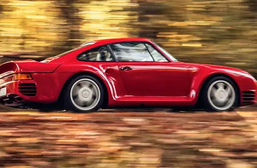 Czerwony Porsche 959 pędzi przez jesienny las, liście tworzą rozmyte smugi.