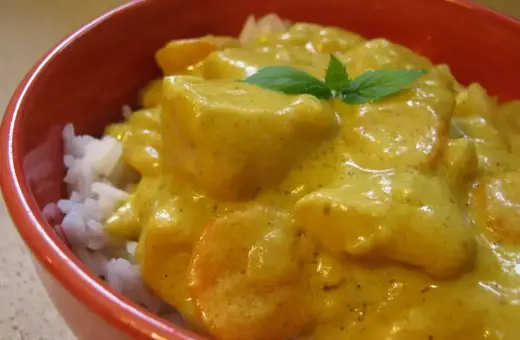 Miseczka ryżu z kurczakiem w kremowym sosie z curry, ozdobiona listkiem mięty.