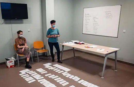 Trening zastępowania agresji: dwie kobiety w maseczkach, tablica z zapiskami, kartki na podłodze.
