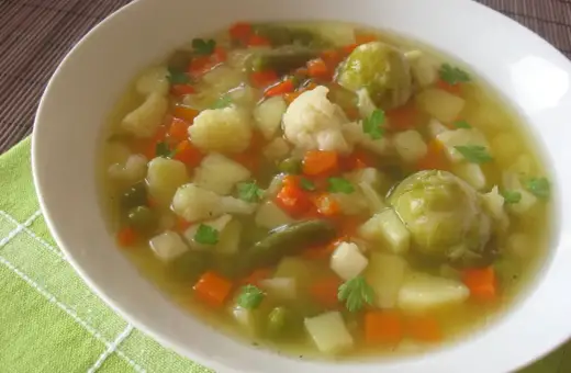 Aromaticzna jarzynowa zupa z ziemniakami, marchewką, kalafiorem i brukselką, udekorowana natką pietruszki.