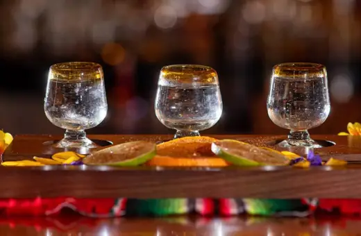 Trzy kieliszki z mezcalem, plasterki limonki i pomarańczy na drewnianej desce.