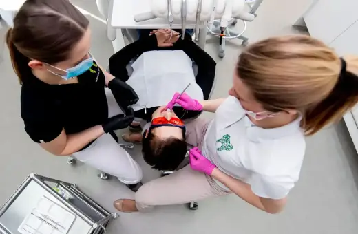 Dwie asystentki stomatologiczne pracują przy pacjencie. Zastanawiasz się, ile zarabia asystentka stomatologiczna?