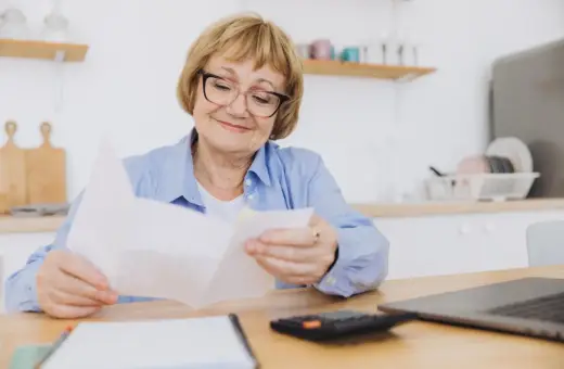 Starsza pani z okularami przegląda dokumenty. Może to rachunki z rp-7 zlikwidowanego zakładu pracy.