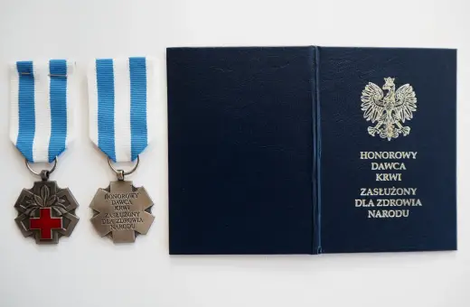 Dwa medale z czerwonym krzyżem i napisem "Honorowy Dawca Krwi Zasłużony dla Zdrowia Narodu" oraz granatowa teczka z godłem Polski.