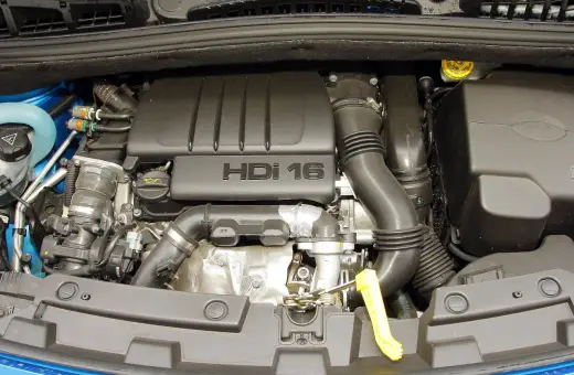Silnik HDI 16 w Citroenie C4. Widoczny jest czarny plastikowy dekiel z napisem "HDI 16", przewody, rury dolotowe i inne elementy jednostki napędowej.