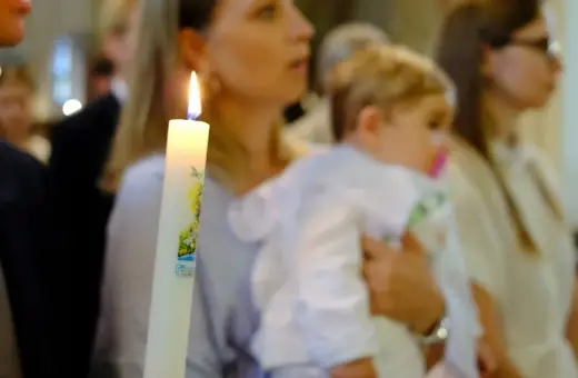 Chrzest dziecka. Czy świadek chrztu musi mieć zaświadczenie? Płonąca świeca chrzcielna w dłoniach.