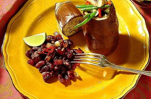 En hel aubergine i ugn, fylld med grönsaker, serveras med en röra av bönor och chili på en gul tallrik.