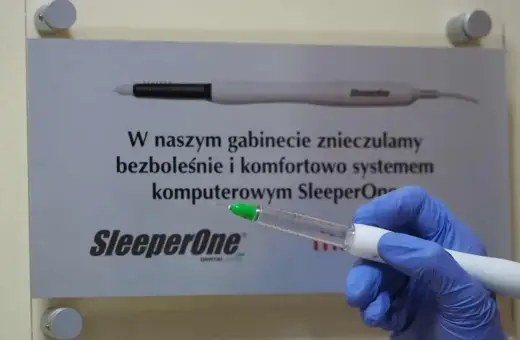 Ręka w niebieskiej rękawiczce trzyma komputerowy system znieczulający SleeperOne. Dowiedz się, ile trzyma znieczulenie u dentysty.
