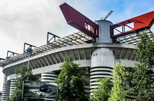 Charakterystyczny stadion Interu Mediolan z czerwonymi elementami konstrukcji i zielenią wokół.