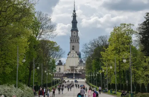 Aleja prowadząca do Jasnej Góry, jednego z najważniejszych sanktuariów maryjnych w Polsce. Ludzie spacerują w kierunku imponującej wieży klasztornej.