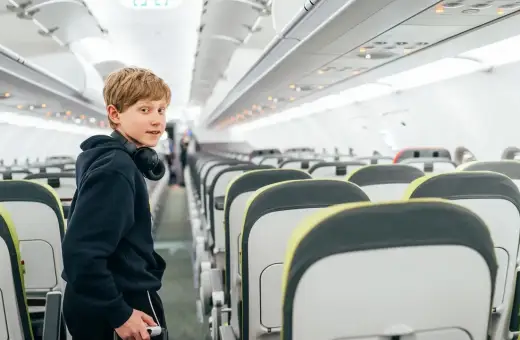 Chłopiec z słuchawkami na szyi w pustym samolocie. Zastanawia się, od ilu lat można latać samemu.