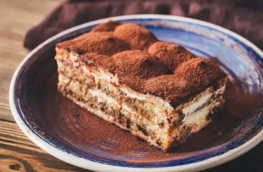 Pyszny kawałek tiramisu z mascarpone, posypany kakao, na talerzu. Idealny sprawdzony przepis na deser.
