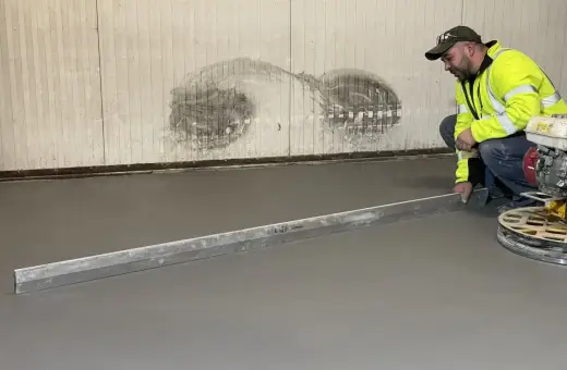 Pracownik w kamizelce odblaskowej wykonuje poziomowanie wylewki betonowej za pomocą łaty.