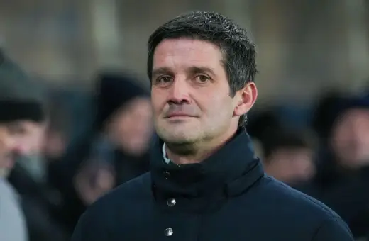 Mężczyzna w ciemnej kurtce, z siwiejącymi włosami, wygląda jak inter trener podczas meczu.