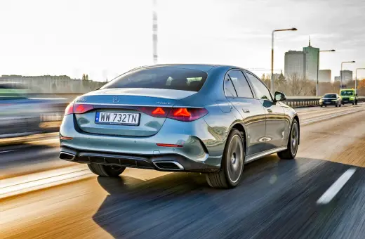Elegancki, błękitny Mercedes E220d 4MATIC pędzi autostradą, mijając miejską panoramę.