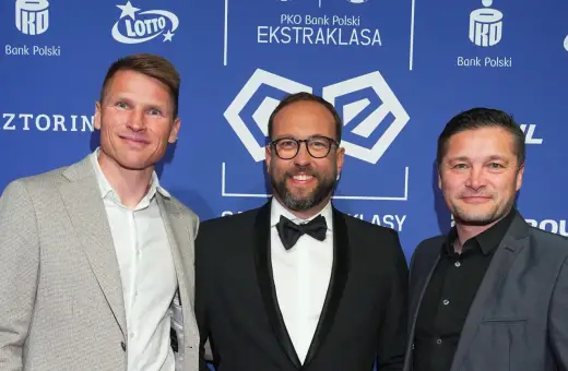 Trzech mężczyzn na tle PKO Bank Polski Ekstraklasa. Jeden z nich, w garniturze, uśmiecha się do obiektywu, być może jako jeden z przyszłych królowie strzelców ekstraklasy.