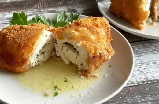 Złocisty kotlet de volaille, przekrojony na pół, odsłaniający soczyste wnętrze z ziołami, pływa w maśle.