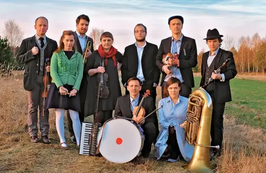 Zespół muzyczny w strojach nawiązujących do stylu folk, z instrumentami: skrzypce, akordeon, bęben, trąbka, klarnet i tuba.