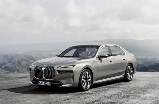 Eleganckie, srebrne BMW 7 2025 z niebieskimi akcentami na felgach, zaparkowane na tle górskiego krajobrazu.