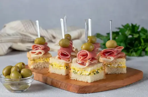 Mini kanapki z szynką, jajkiem i oliwkami na drewnianej desce. Idealne finger food na przyjęcie.