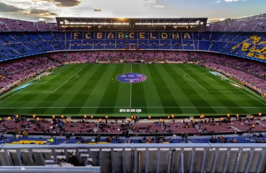 Widok na murawę i trybuny stadionu FC Barcelona Camp Nou. Słońce zachodzi nad stadionem.