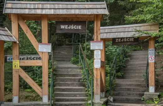 Kamienne schody prowadzą do wejścia na trasę turystyczną w Szczelińcu Wielkim. Po prawej stronie znajduje się znak "Zejście" i zakaz wchodzenia pod prąd.
