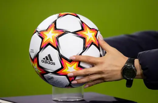 Dłoń z zegarkiem trzyma piłkę Adidas z gwiazdami, gotową do gry w ulubionym klubie piłkarskim na boisku.