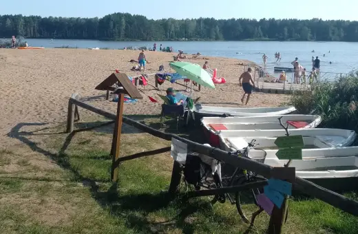Słoneczny dzień nad zalewem zielona. Ludzie odpoczywają na plaży, kąpią się w wodzie, a obok cumują łódki.