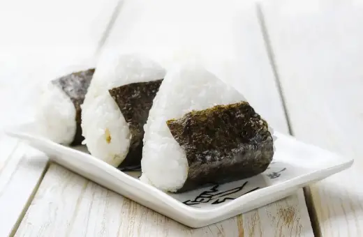 Trzy ryżowe kulki onigiri z nori na białym talerzyku. Idealne na szybki lunch, gdy szukasz prostego onigiri przepis.