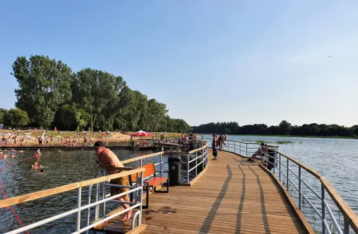 Ludzie odpoczywają i kąpią się nad zalewem Borki. Drewniane molo zaprasza do spacerów i podziwiania widoków.