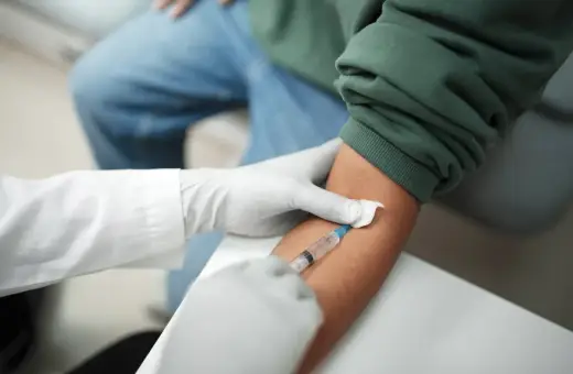 Pobieranie krwi do badań, które mogą pomóc w diagnostyce trzustki. Lekarz w rękawiczkach pobiera krew strzykawką.