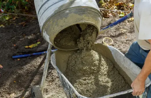 Beton z samego piasku i cementu wylewa się z betoniarki do taczki.