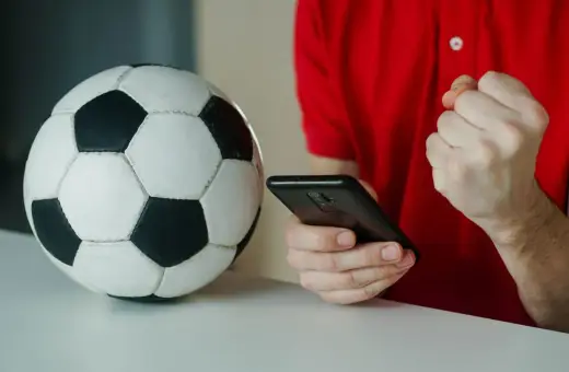 Piłka nożna i smartfon. Kibic sprawdza wynik, licząc na powyżej 2.5 gola.