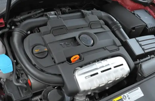 Silnik 1.4 TSI z widocznym logo VW. Czarna pokrywa silnika z napisem TSI i pomarańczową pętlą do sprawdzania oleju.