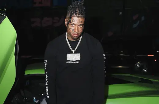 Raper z tatuażami na twarzy, znany jako blueface, pozuje obok jaskrawozielonego samochodu sportowego.