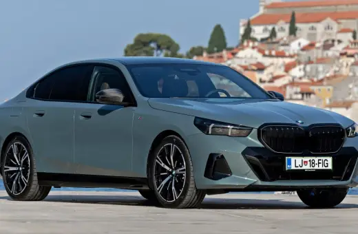 Szary BMW 520 z czarnymi felgami stoi na tle malowniczego nadmorskiego miasteczka.