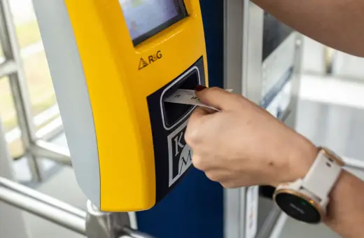 Ręka z zegarkiem wkłada bilet godzinny Kraków do żółtego automatu.