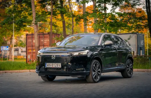 Elegancki, czarny Honda HR-V 2025 na tle jesiennych drzew i kontenerów.