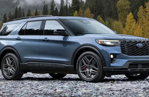 Niebieski Ford Explorer ST zaparkowany na kamienistej plaży, z jesiennym lasem w tle.